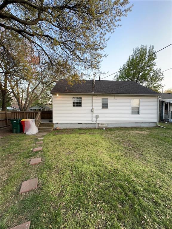 back of property with a shingled roof, crawl space, fence, and a lawn