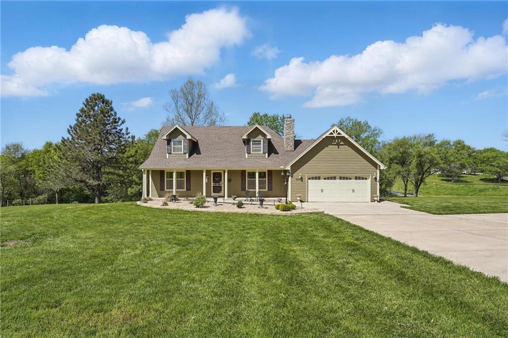 cape cod-style house featuring driveway, a garage, a porch, and a front yard