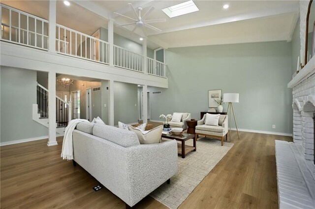 living room with a fireplace, baseboards, stairway, high vaulted ceiling, and ceiling fan with notable chandelier
