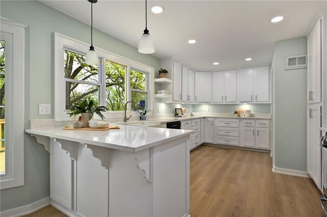 kitchen featuring a sink, a peninsula, white cabinetry, and visible vents
