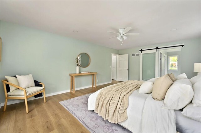 bedroom featuring light wood-style floors, baseboards, a barn door, and visible vents