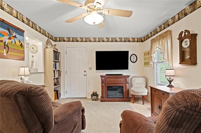 living area featuring a glass covered fireplace, a ceiling fan, and light tile patterned floors
