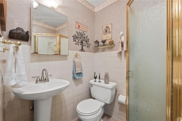 bathroom featuring a shower stall, wallpapered walls, wainscoting, tile walls, and toilet