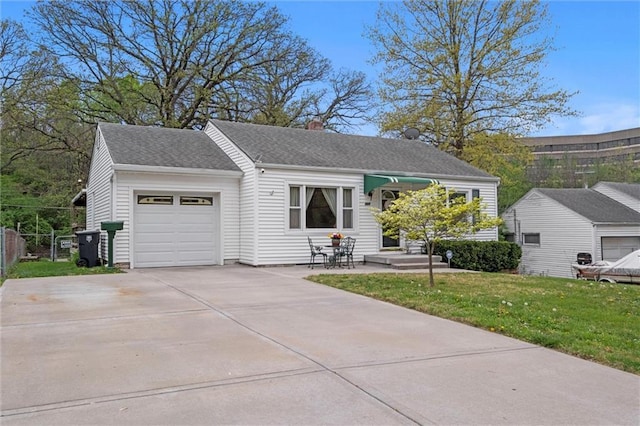 view of front of house with fence, concrete driveway, an attached garage, roof with shingles, and a front yard