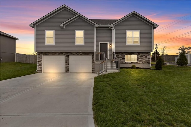 bi-level home with a lawn, stone siding, concrete driveway, and a garage