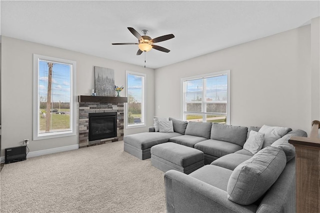 carpeted living area with a stone fireplace, baseboards, and ceiling fan