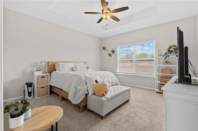 bedroom featuring a raised ceiling, a ceiling fan, baseboards, and light carpet