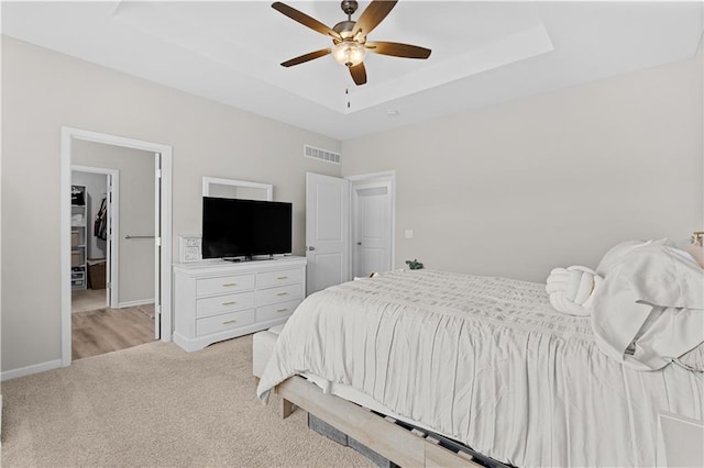 bedroom featuring a tray ceiling, visible vents, light carpet, baseboards, and ceiling fan