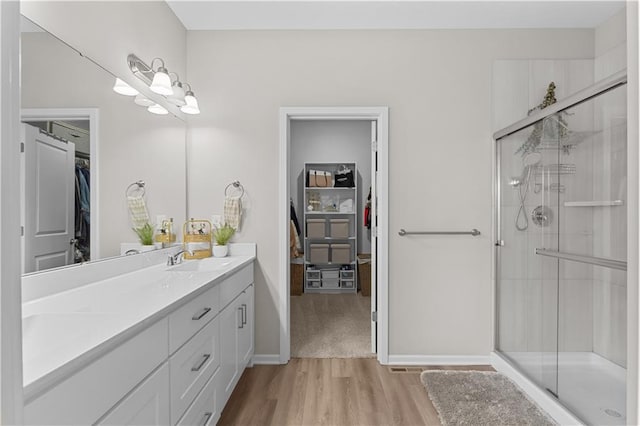 bathroom with wood finished floors, vanity, a walk in closet, and a stall shower