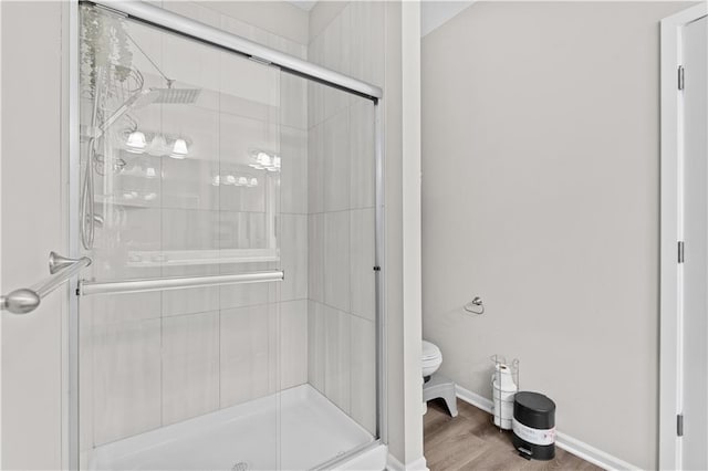 bathroom featuring baseboards, toilet, wood finished floors, and a stall shower