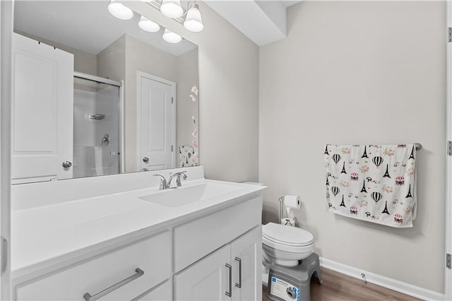 bathroom with wood finished floors, toilet, vanity, baseboards, and a stall shower