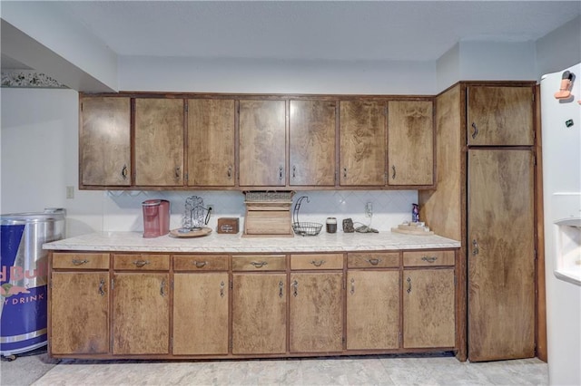 kitchen featuring brown cabinetry, light countertops, tasteful backsplash, and white refrigerator with ice dispenser