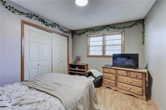 bedroom featuring light wood-style flooring, baseboards, a textured ceiling, and a closet