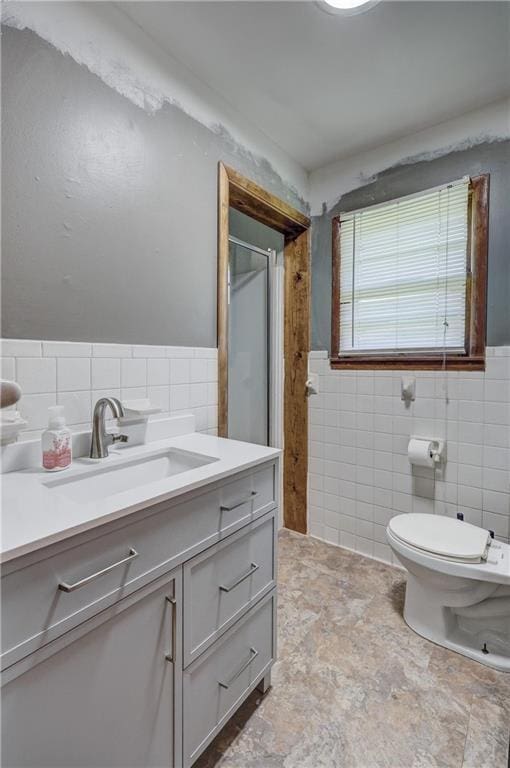 bathroom featuring wainscoting, vanity, a shower with shower door, and tile walls