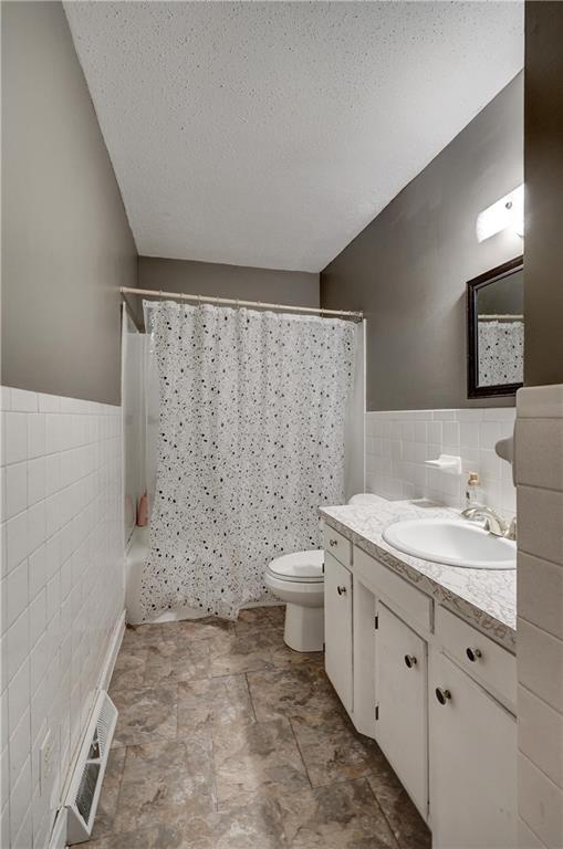 bathroom with a textured ceiling, vanity, tile walls, a wainscoted wall, and toilet