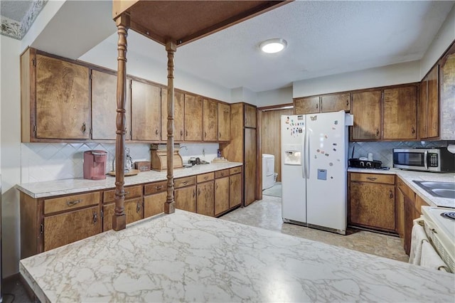 kitchen with stainless steel microwave, brown cabinetry, white refrigerator with ice dispenser, and washer / dryer