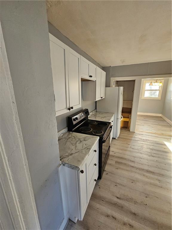 4410 Myrtle Ave, Kansas City, MO 64130 - kitchen featuring black electric range oven, light wood-style floors, light countertops, white cabinets, and freestanding refrigerator