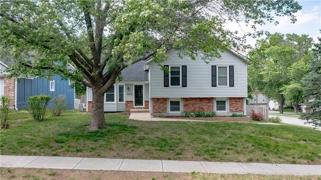 tri-level home with a front yard, brick siding, and central air condition unit