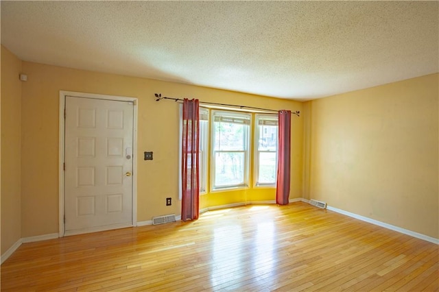 spare room featuring light wood-style floors, a textured ceiling, and baseboards