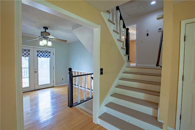 stairway featuring french doors, ceiling fan, wood finished floors, baseboards, and a textured ceiling