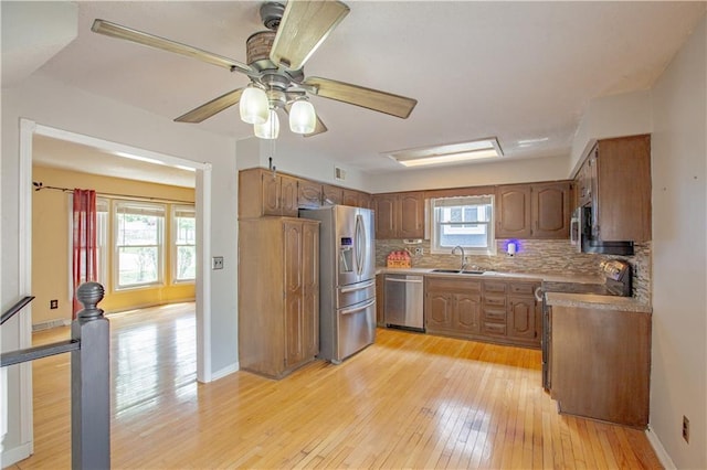 kitchen featuring appliances with stainless steel finishes, light wood-type flooring, tasteful backsplash, a sink, and baseboards