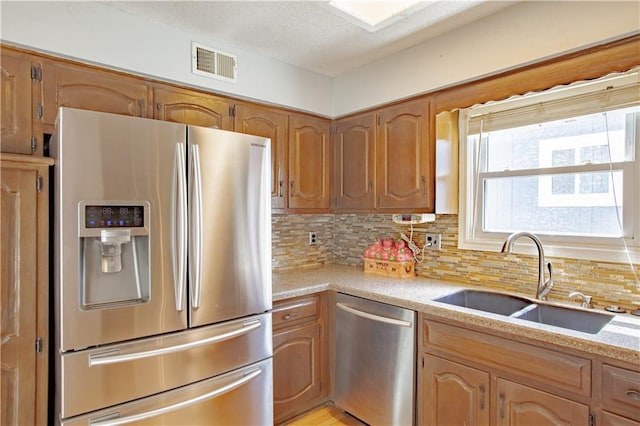 kitchen featuring stainless steel appliances, a sink, backsplash, brown cabinets, and a textured ceiling