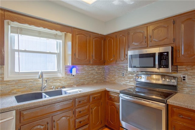 kitchen featuring stainless steel appliances, a sink, light countertops, backsplash, and brown cabinets
