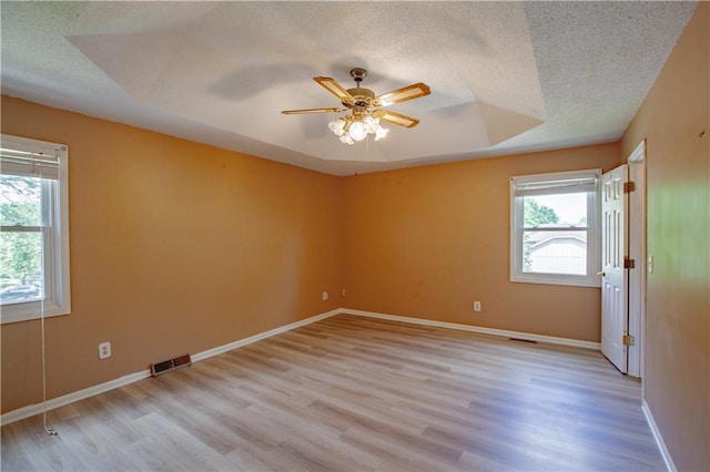 empty room with healthy amount of natural light, light wood-style flooring, a ceiling fan, and a textured ceiling