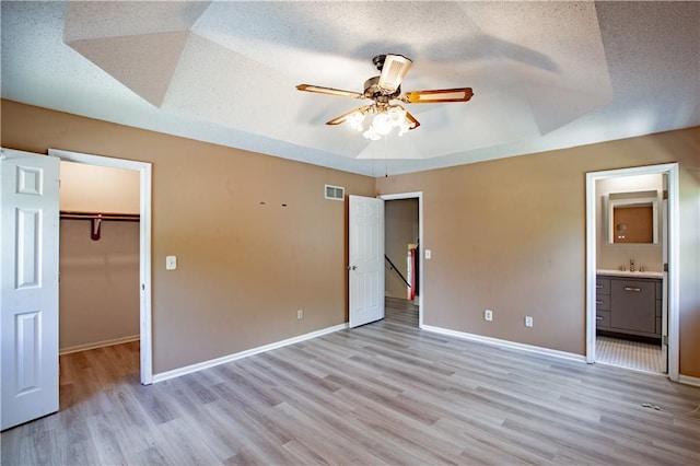 unfurnished bedroom with light wood-style floors, a spacious closet, a sink, a tray ceiling, and a closet