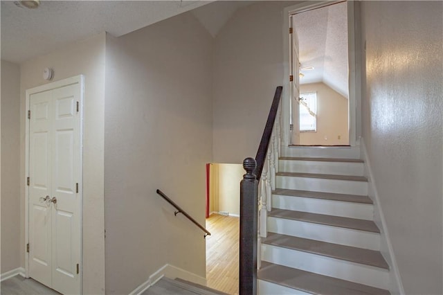 stairway featuring lofted ceiling, a textured ceiling, wood finished floors, and baseboards