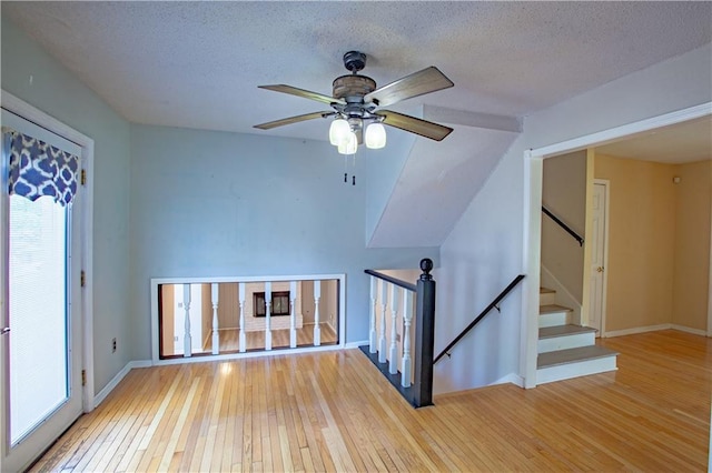 unfurnished living room featuring wood-type flooring, ceiling fan, a textured ceiling, and baseboards
