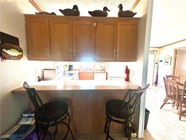 171 E 5th St, Schell City, MO 64783 - kitchen featuring brown cabinetry, white dishwasher, a peninsula, and a kitchen breakfast bar