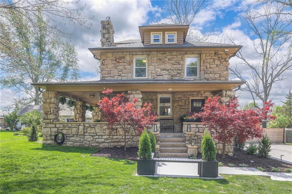 view of front of house featuring a chimney, a porch, a front lawn, and stone siding