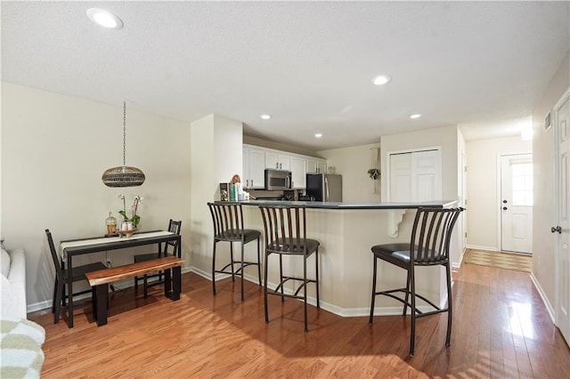 kitchen featuring white cabinets, light wood-style floors, baseboards, a kitchen bar, and appliances with stainless steel finishes