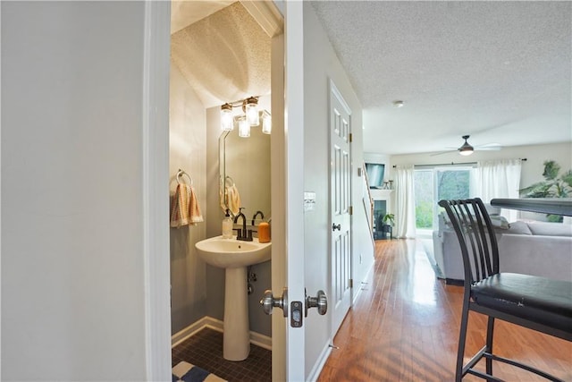 hall with baseboards, wood finished floors, and a textured ceiling