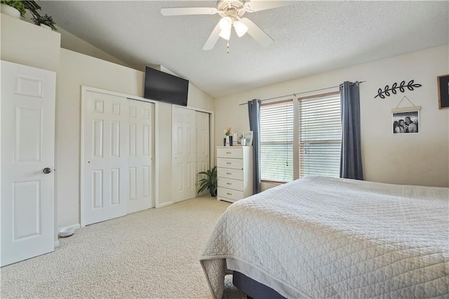 bedroom with lofted ceiling, multiple closets, carpet, and a textured ceiling