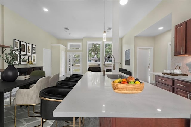kitchen featuring dark brown cabinets, a sink, a kitchen island with sink, light countertops, and visible vents
