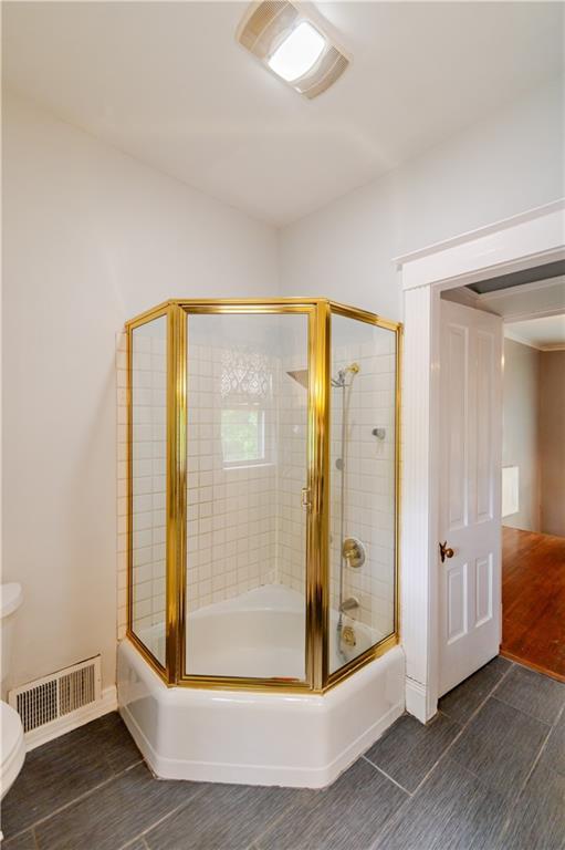 603 N 5th St, Atchison, KS 66002 - full bathroom featuring wood finished floors, toilet, combined bath / shower with glass door, and baseboards
