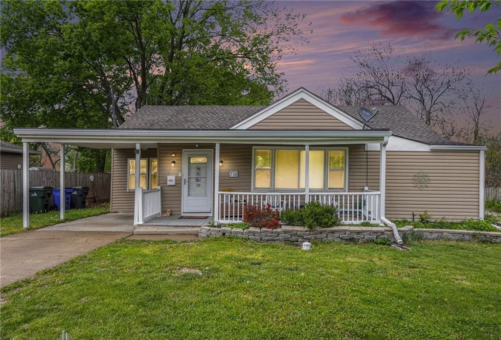view of front facade featuring a porch, fence, a shingled roof, and a front yard
