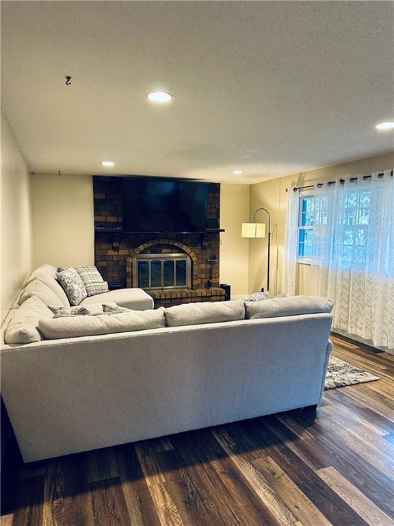 living area featuring a brick fireplace, recessed lighting, and dark wood finished floors