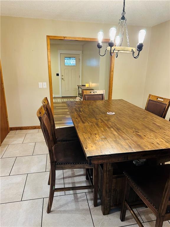 dining space featuring a textured ceiling, baseboards, an inviting chandelier, and light tile patterned floors