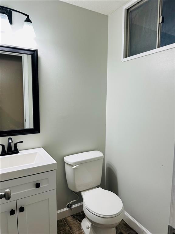 half bath with baseboards, toilet, and vanity