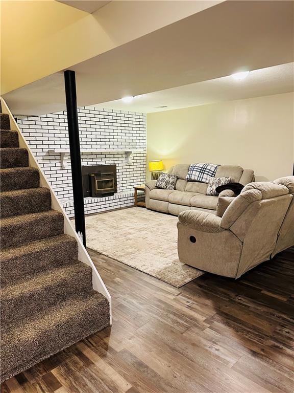 living room featuring stairs, a brick fireplace, and wood finished floors