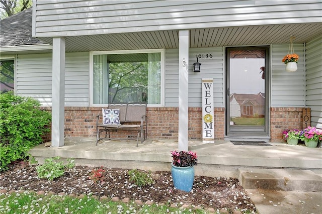 doorway to property featuring roof with shingles, covered porch, and brick siding