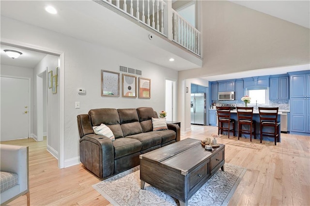 living room featuring light wood-type flooring, baseboards, a high ceiling, and visible vents