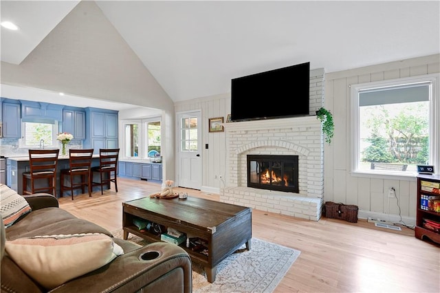living area with light wood finished floors, a brick fireplace, a decorative wall, and high vaulted ceiling