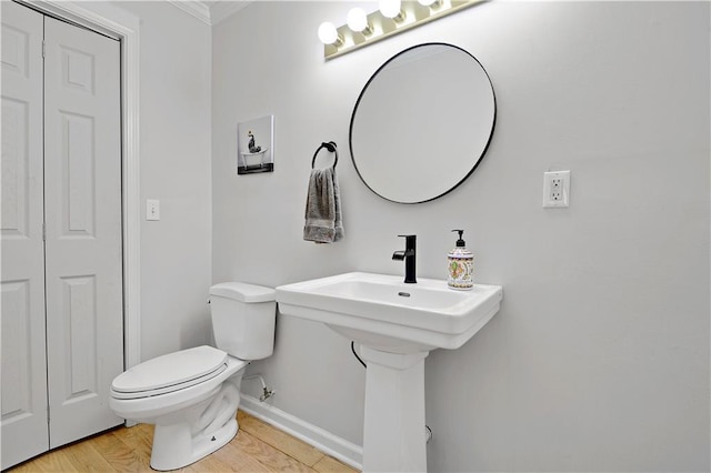 half bathroom with baseboards, crown molding, wood finished floors, and toilet