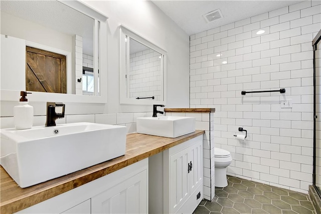 full bathroom featuring visible vents, a sink, toilet, and tile walls