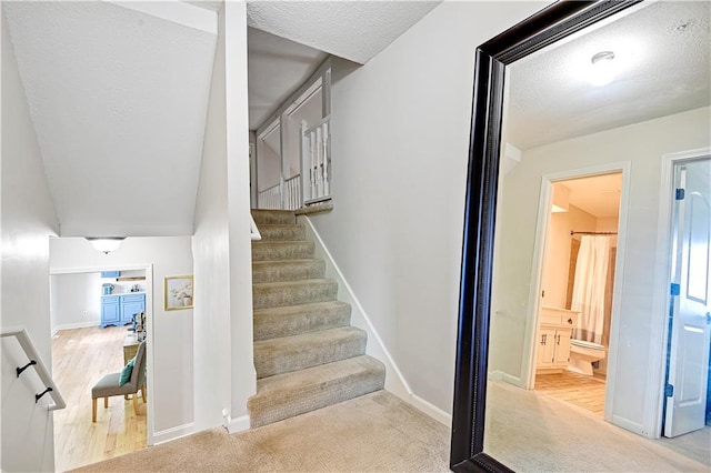 staircase with baseboards, carpet flooring, and a textured ceiling
