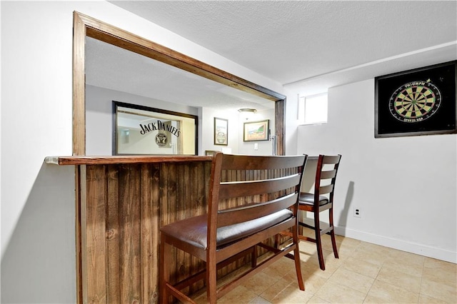 interior space with a bar, a textured ceiling, and baseboards